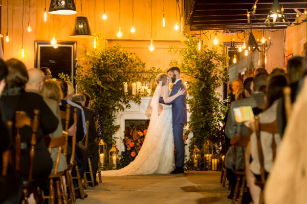 Sunset wedding ceremony - bride and groom kiss in front of fireplace in barn