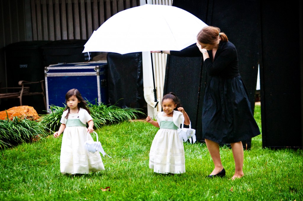 wedding planner holding an umbrella over the flower girls as they walk to the wedding ceremony